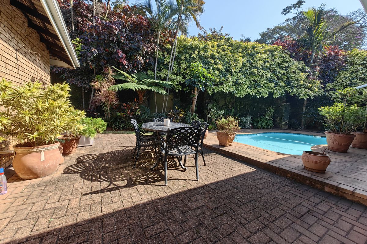 A private outdoor pool area featuring brick paving and lush, established garden landscaping, providing a tranquil space for relaxation and outdoor entertainment.
