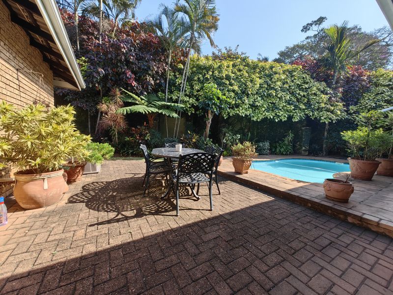 A private outdoor pool area featuring brick paving and lush, established garden landscaping, providing a tranquil space for relaxation and outdoor entertainment.