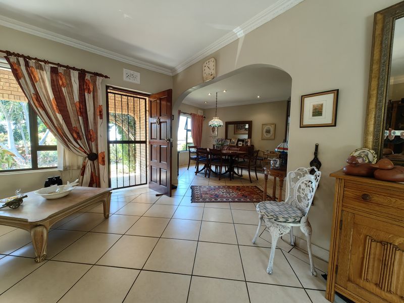Open plan living and dining area featuring tiled flooring, decorative crown molding, and an arched transition between spaces with access to an outdoor patio.