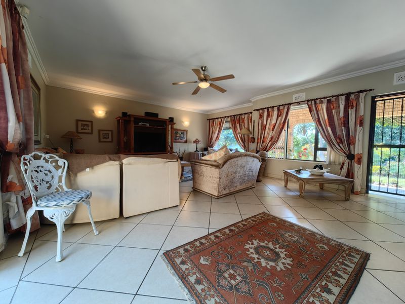 Spacious living room featuring tiled flooring, ceiling fan, and large windows with access to the exterior through a security gate.