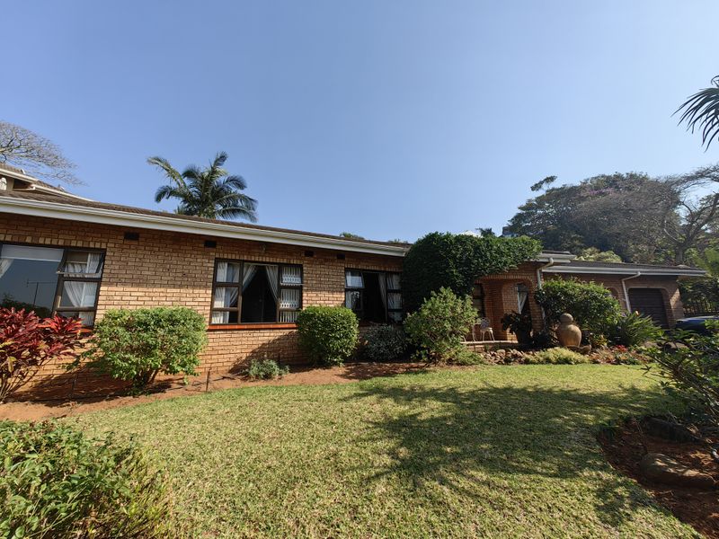 A well-maintained single-story brick house featuring a landscaped front garden, aluminum window frames, and a covered entrance area.
