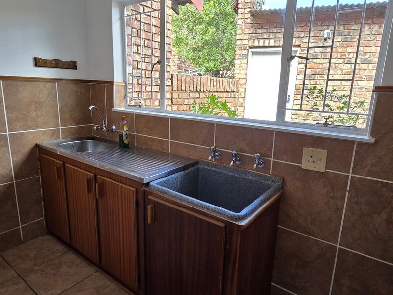 A functional laundry area featuring built-in cabinetry, a stainless steel sink, a deep utility basin, and tiled wall finishes with a window view.