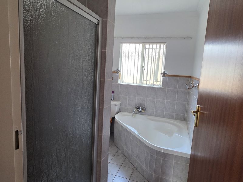 A functional bathroom featuring a corner bathtub, separate shower enclosure, and tiled finishes, offering a clean and practical layout.