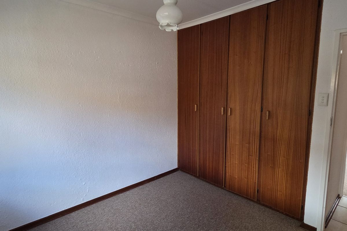 An empty bedroom featuring built-in wooden cupboards, carpeted flooring, and a coved ceiling, offering a blank canvas for potential updates.