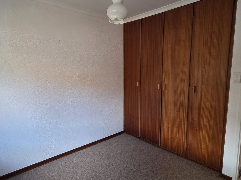 An empty bedroom featuring built-in wooden cupboards, carpeted flooring, and a coved ceiling, offering a blank canvas for potential updates.