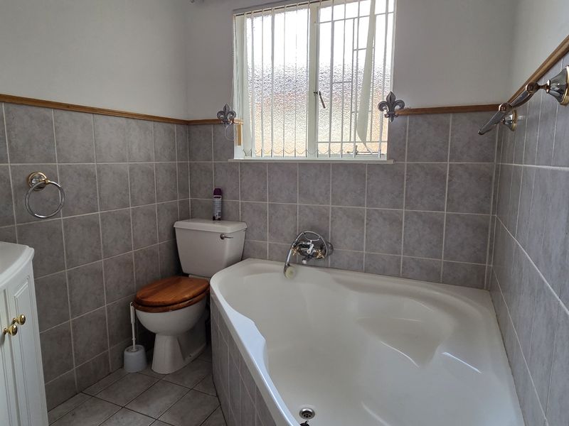 A functional bathroom featuring a corner bathtub, vanity cabinet, and neutral ceramic tiling throughout.