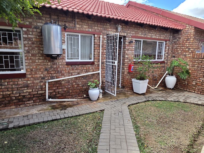 Rear exterior view of the townhouse featuring face brick walls, a tiled roof, security gates, and a paved garden walkway.