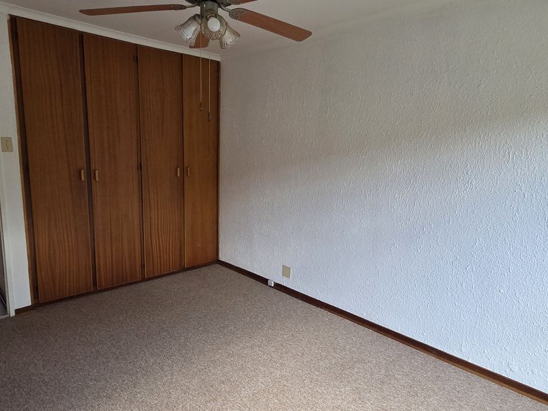 A vacant bedroom featuring built-in wooden cupboards, a ceiling fan, and carpeted flooring, offering a blank canvas for potential updates.