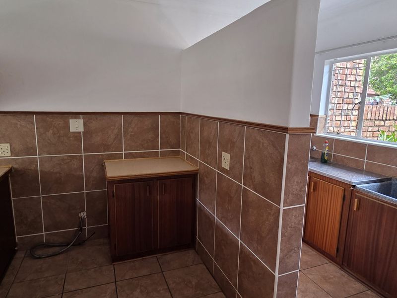 A functional scullery area featuring built-in wooden cabinetry, laminate countertops, a utility sink, and tiled finishes throughout.