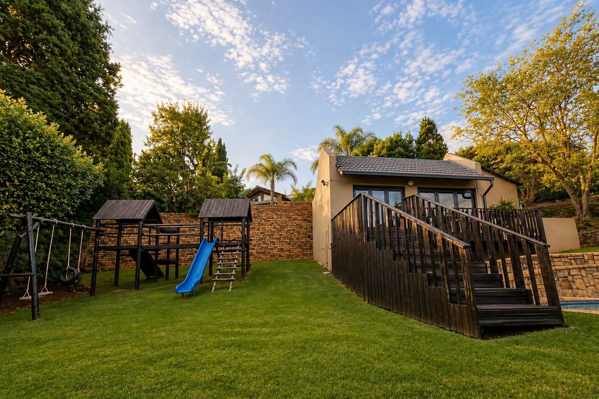 Rear garden view featuring a well-maintained lawn, timber deck with staircase, and a stone retaining wall, providing a functional outdoor living space.