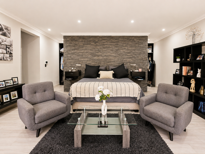 Spacious bedroom featuring a textured stone feature wall, integrated built-in wardrobes, recessed downlighting, and modern light-toned flooring.