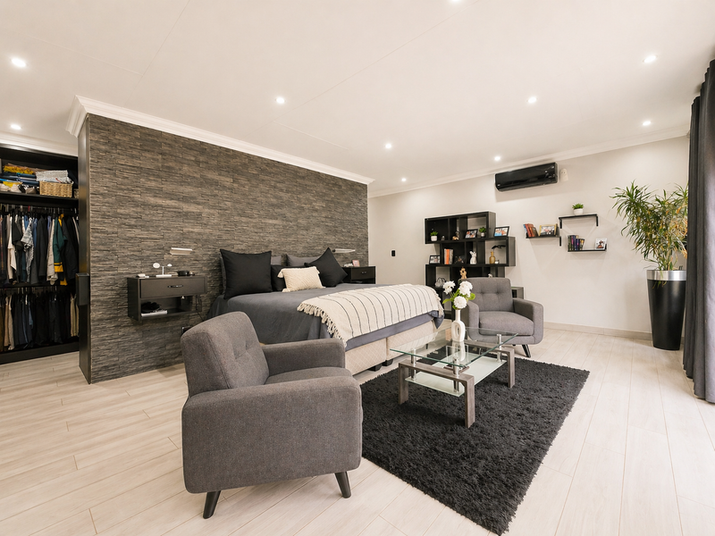 Spacious master bedroom featuring a modern stone accent wall, built-in wardrobe, tiled flooring, and integrated air conditioning.