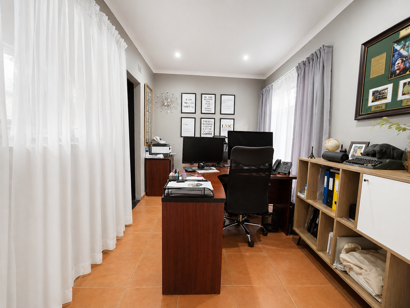 A functional home office space featuring ceramic floor tiles, recessed downlighting, and large windows dressed with curtains.