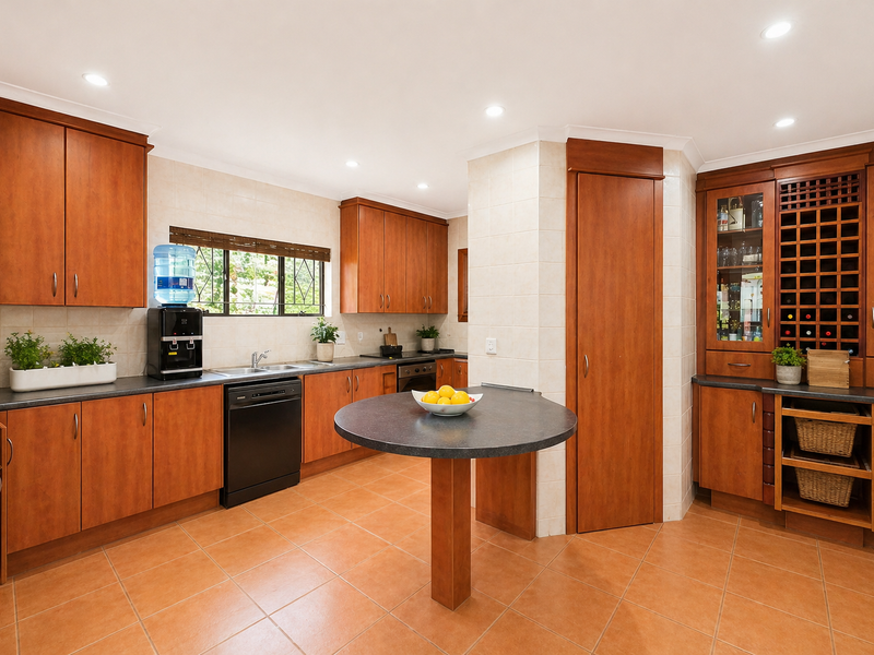 A well-maintained kitchen featuring warm-toned wooden cabinetry, ample counter space, a central breakfast bar, and integrated wine storage.