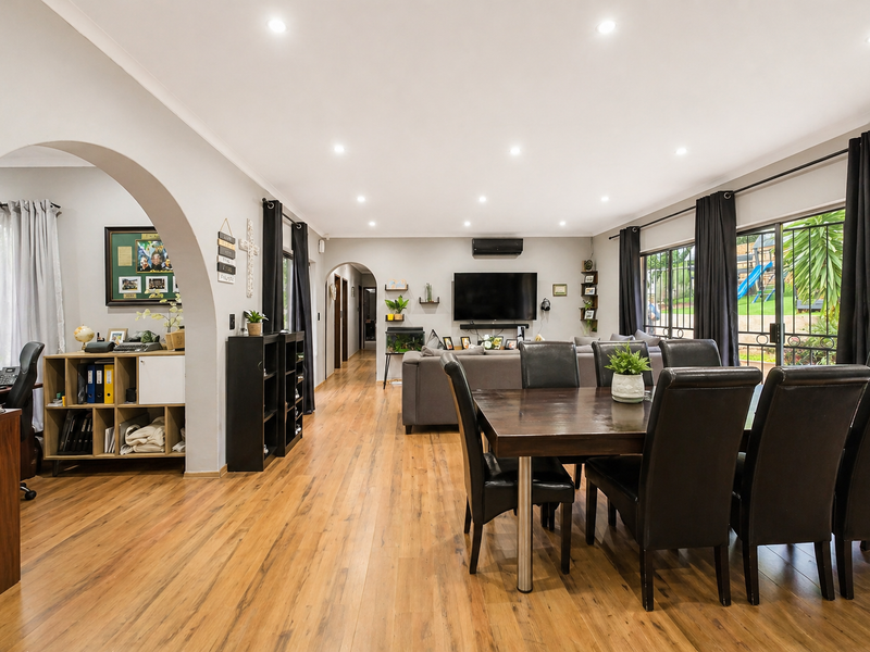 Spacious open-plan living and dining area featuring laminate flooring, recessed downlighting, and large sliding glass doors leading to the exterior.