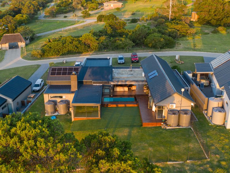 Aerial view of a modern residential property featuring solar panels, a swimming pool, timber decking, and multiple water storage tanks in a landscaped setting.