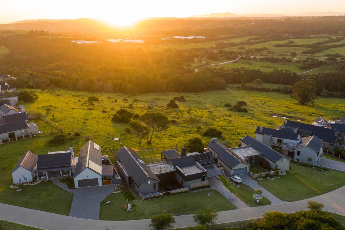 Aerial view of a modern residential estate featuring homes with pitched roofs, solar panels, and paved driveways set against a scenic rural landscape.