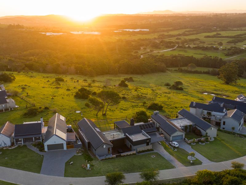 Aerial view of a modern residential estate featuring homes with pitched roofs, solar panels, and paved driveways set against a scenic rural landscape.