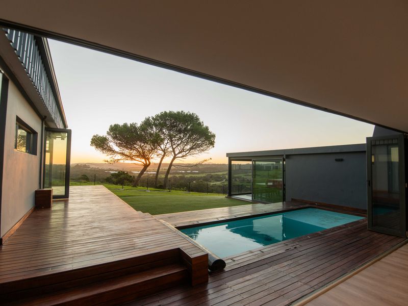 Modern outdoor entertainment area featuring timber decking, a swimming pool, and expansive bi-fold doors opening to a scenic landscape view.