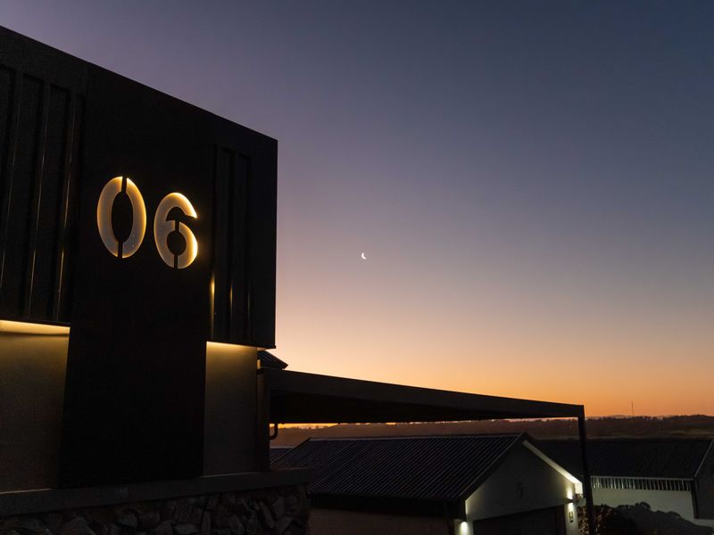 A striking modern architectural facade featuring illuminated house numbering and high-quality metal and stone finishes at dusk.