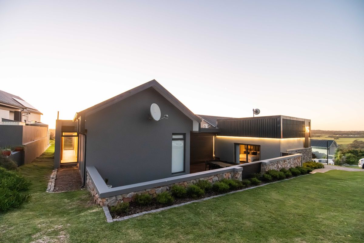 Modern rear elevation featuring stone cladding, integrated LED lighting, and a landscaped garden with a retaining wall.
