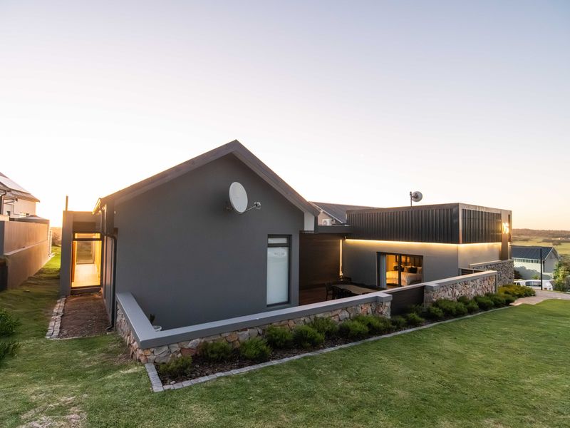 Modern rear elevation featuring stone cladding, integrated LED lighting, and a landscaped garden with a retaining wall.