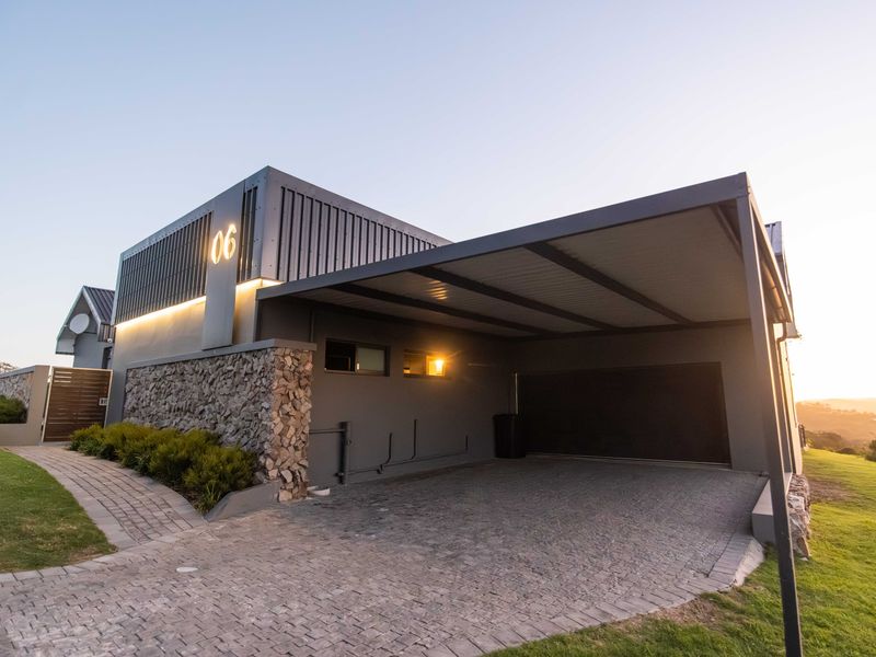 Modern front elevation featuring a spacious carport, stone cladding accents, paved driveway, and integrated exterior lighting.
