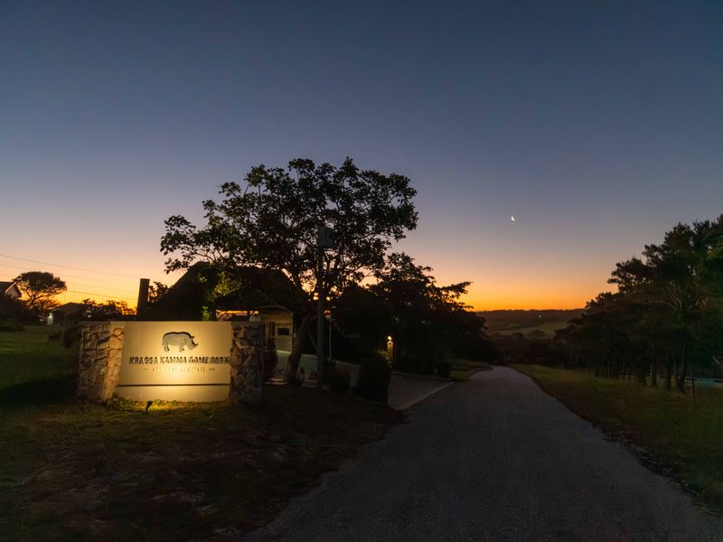 Entrance view of Kragga Kamma Game Park residential estate at dusk, featuring stone-clad signage and a paved driveway.