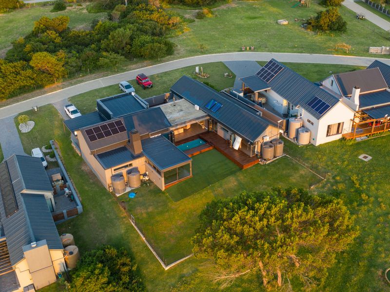 Aerial view of a modern residential property featuring solar panels, a swimming pool, timber decking, and multiple water storage tanks on a landscaped lot.