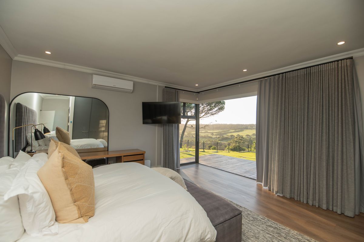 Spacious bedroom featuring modern finishes, air conditioning, and large sliding doors opening onto a private timber deck with scenic landscape views.