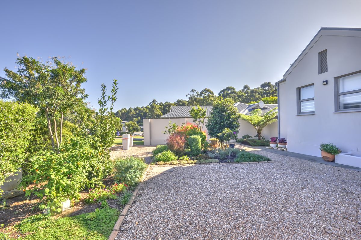 A well-maintained rear garden area featuring a gravel driveway, landscaped garden beds, and a clean exterior building facade.