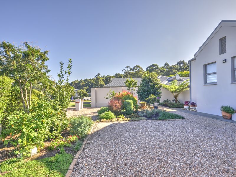 A well-maintained rear garden area featuring a gravel driveway, landscaped garden beds, and a clean exterior building facade.