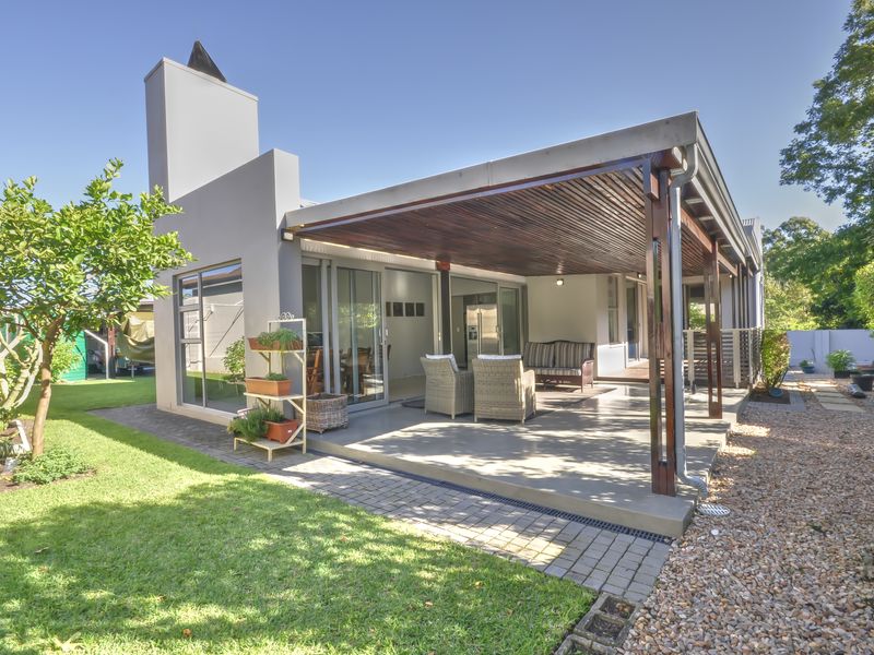 A spacious covered patio featuring a timber pergola, concrete flooring, and an external fireplace, seamlessly connecting to the interior living space via sliding glass doors.