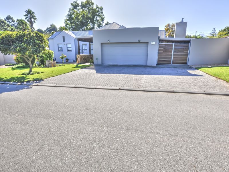 Front elevation of a modern house featuring a paved driveway, automated garage door, and secure gated entrance with a well-maintained front garden.