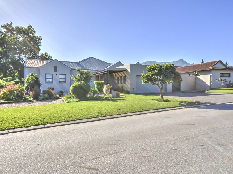 A well-maintained single-story residential property featuring a metal roof, paved driveway, integrated garage, and a neatly landscaped front garden.