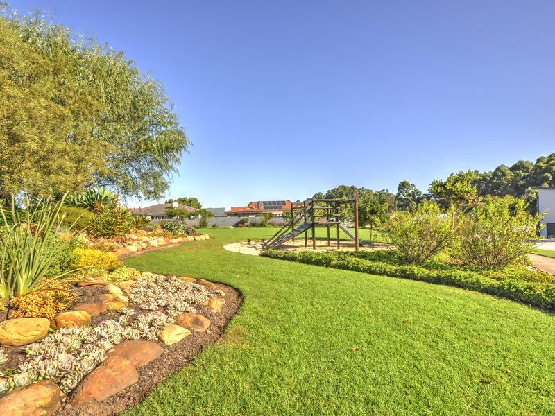 A well-maintained landscaped garden featuring a lush lawn, rockery borders, and a dedicated playground area within a spacious outdoor setting.