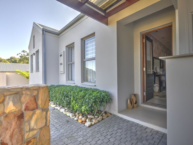 Front entrance area featuring a paved walkway, stone feature wall, and timber pergola over the doorway.