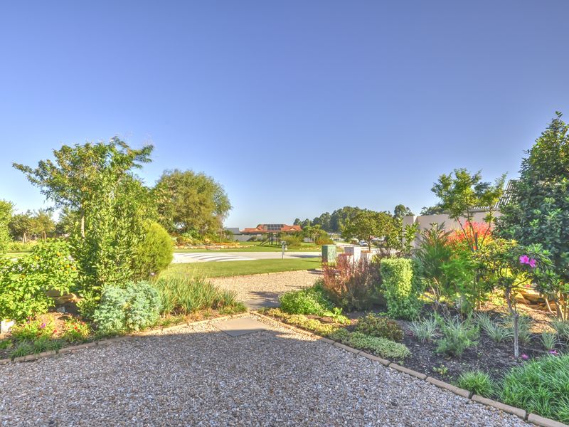 A well-maintained front garden featuring a gravel driveway, established shrubs, and landscaped garden beds under a clear blue sky.