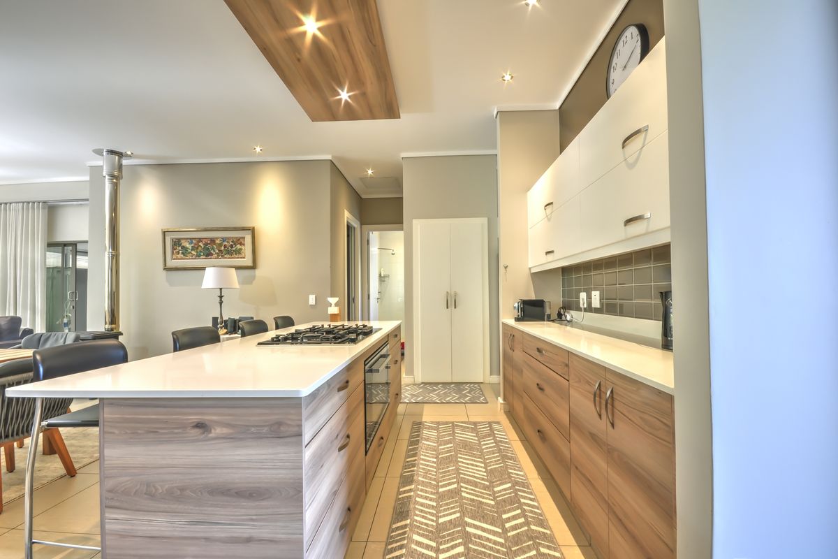 Modern kitchen featuring a central island with gas hob, built-in oven, stone countertops, and sleek wood-finish cabinetry with integrated lighting.