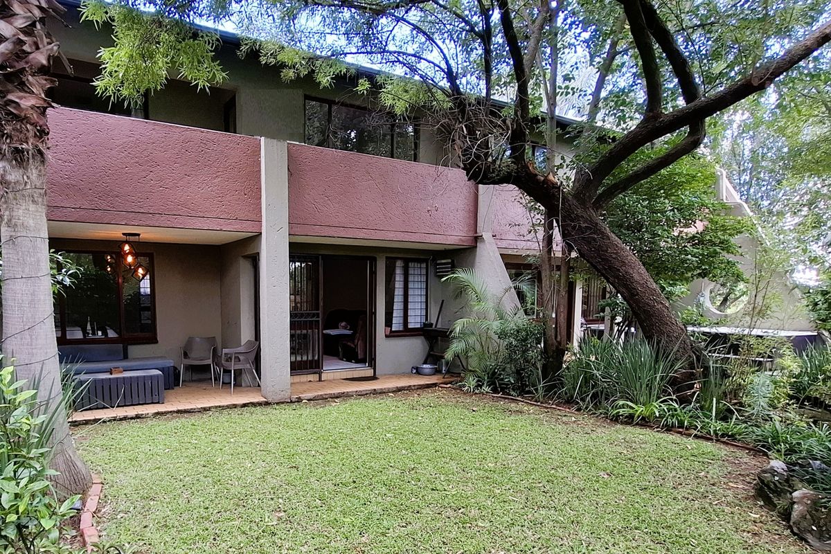 Rear view of the apartment featuring a covered patio area, sliding glass doors, and a private garden with mature trees.