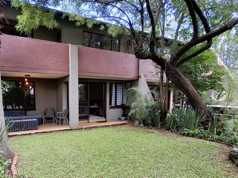 Rear view of the apartment featuring a covered patio area, sliding glass doors, and a private garden with mature trees.