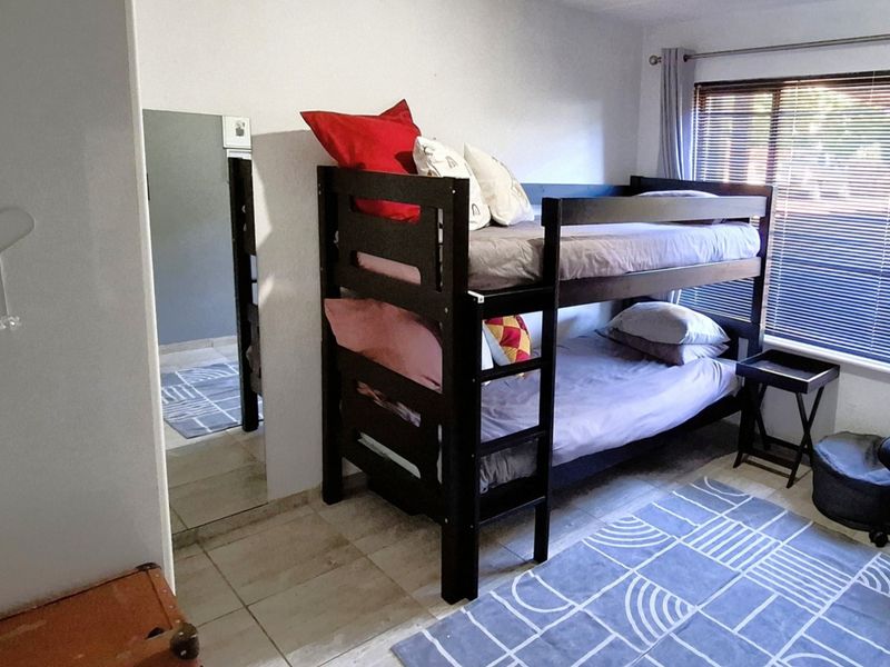 A functional bedroom featuring tiled flooring, a large window with venetian blinds, and a built-in mirror.