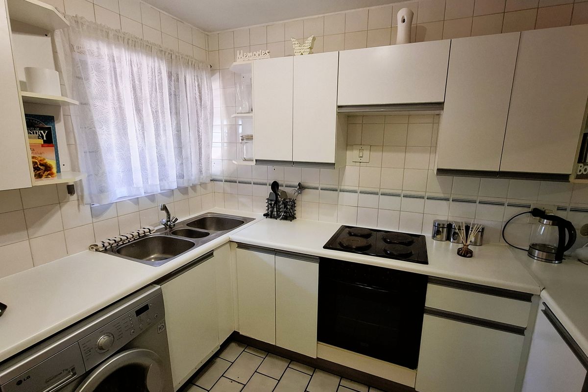 Functional kitchen featuring white cabinetry, tiled backsplash, double sink, built-in oven, and electric hob with space for a washing machine.
