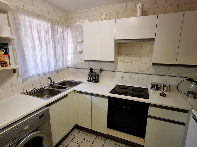 Functional kitchen featuring white cabinetry, tiled backsplash, double sink, built-in oven, and electric hob with space for a washing machine.