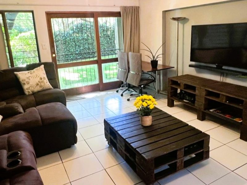 A bright living room featuring white tiled flooring and a large sliding glass door with security gate, providing direct access to the garden area.