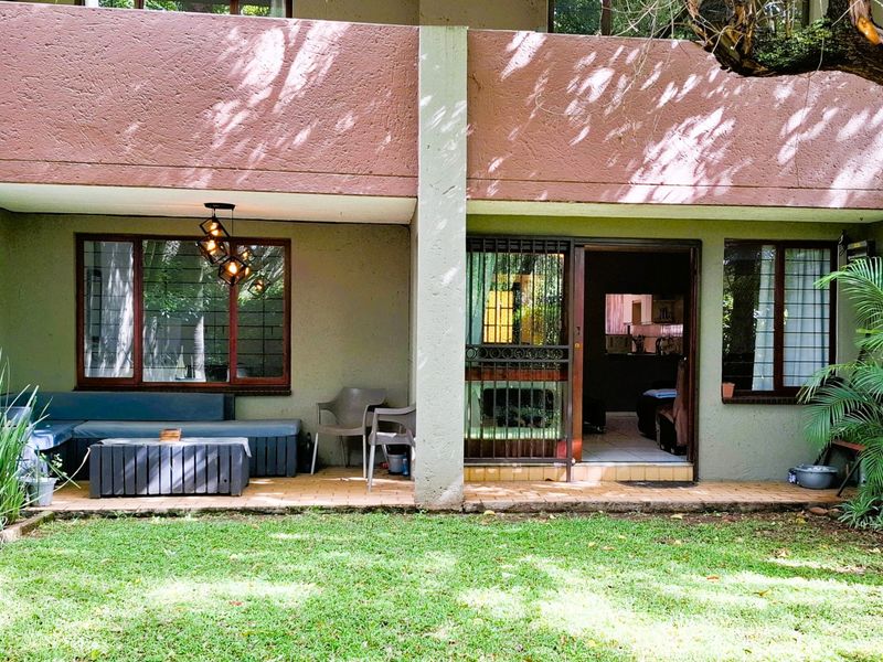 A ground-floor apartment patio featuring tiled flooring, security gate access, and direct entry into the living space, overlooking a private garden area.
