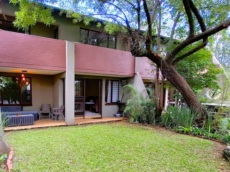 Rear view of the apartment featuring a covered patio, sliding glass doors, and a private garden area with mature trees.