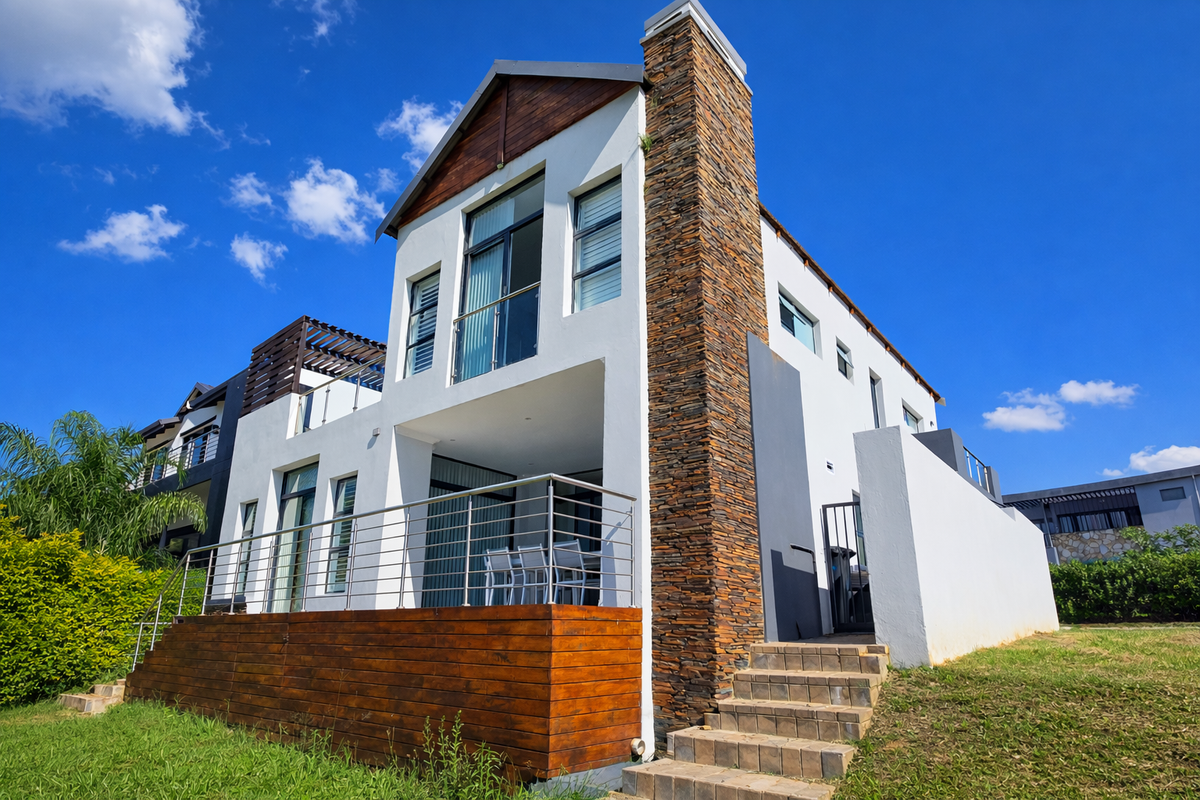 Rear view of a modern multi-level home featuring a stone-clad chimney, timber decking, and a covered patio with stainless steel balustrades.