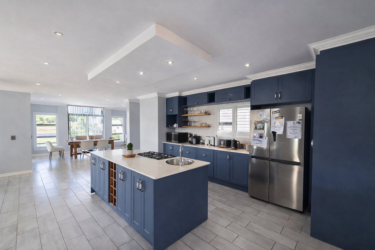 Spacious open-plan kitchen featuring a large central island with gas cooktop, modern blue cabinetry, stone countertops, and sleek tiled flooring.