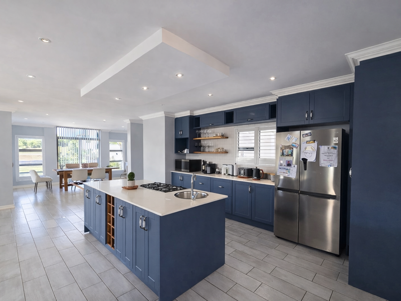 Spacious open-plan kitchen featuring a large central island with gas cooktop, modern blue cabinetry, stone countertops, and sleek tiled flooring.
